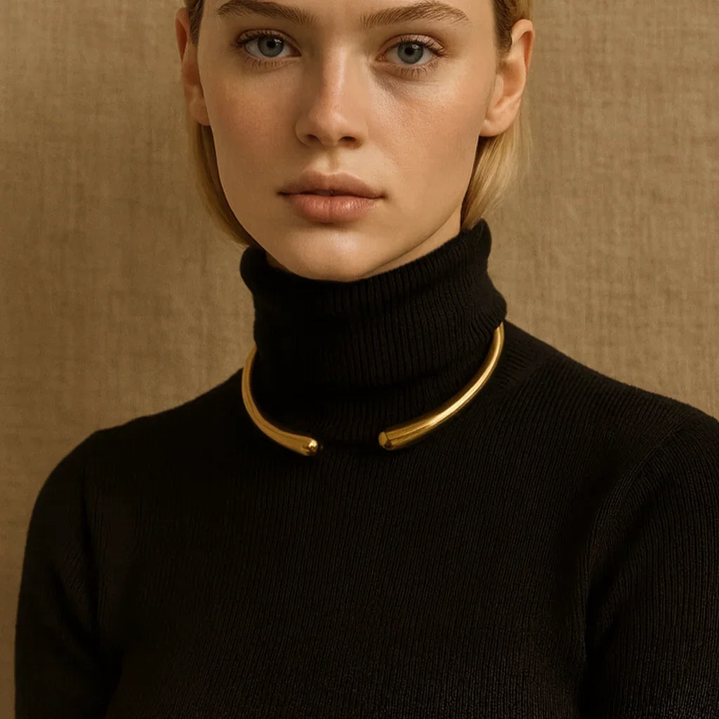Woman wearing a black turtleneck with a gold collar against a beige background