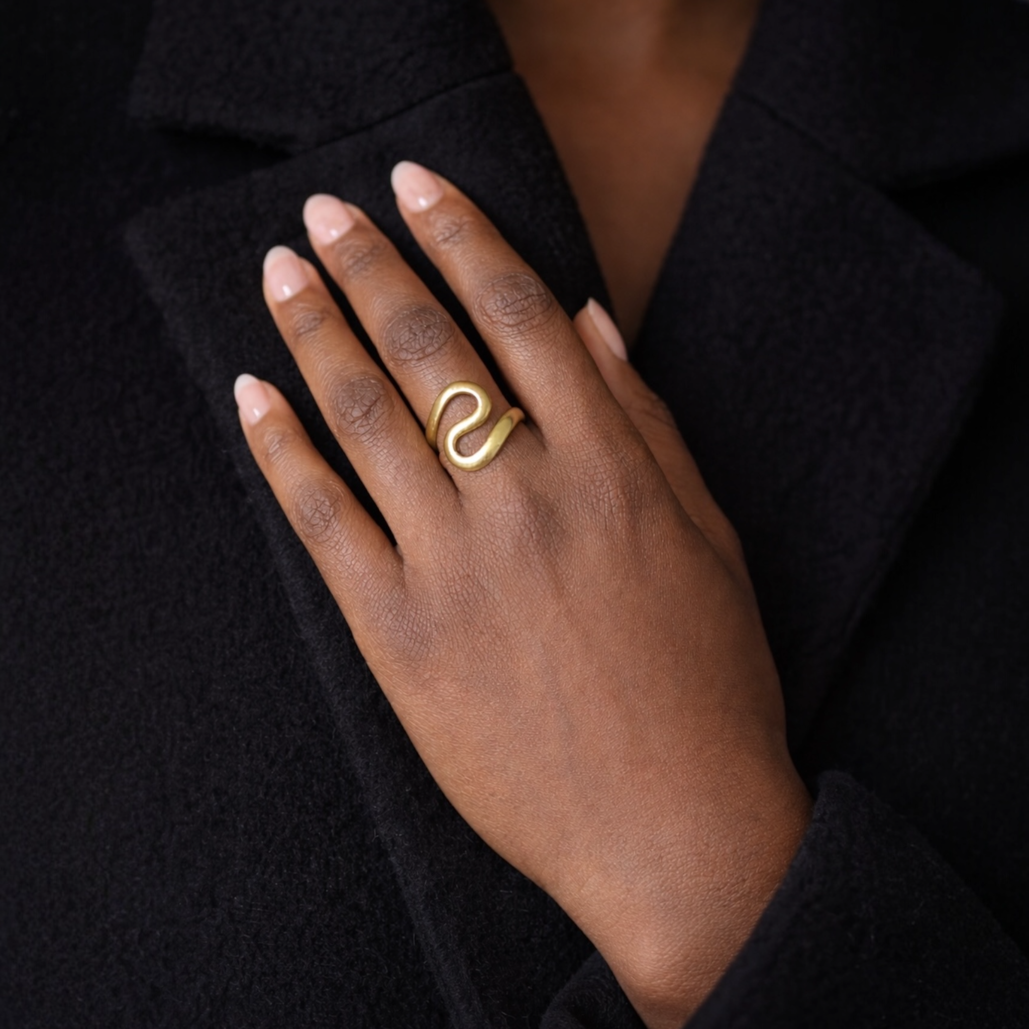 Hand wearing a gold ring with a 'S' design against a dark background