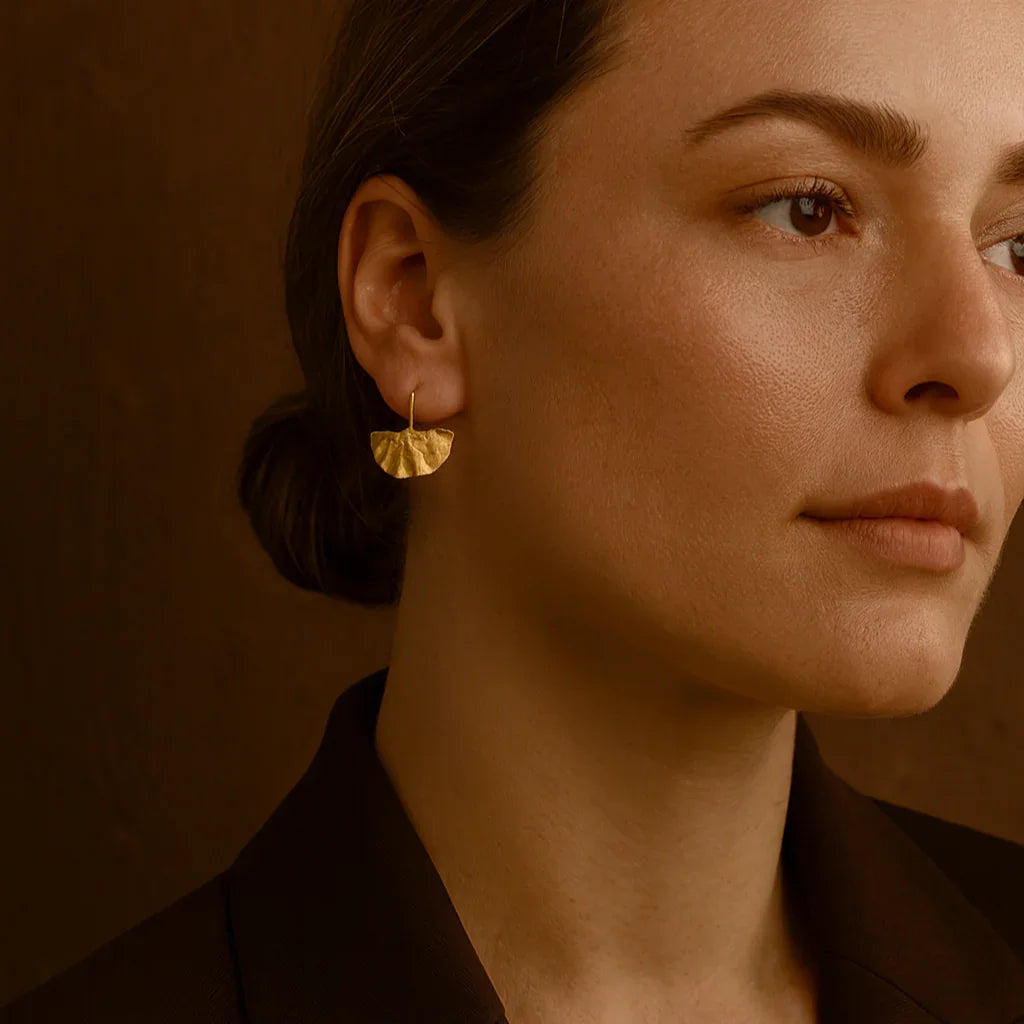 Close-up of a woman wearing gold earrings against a warm brown background