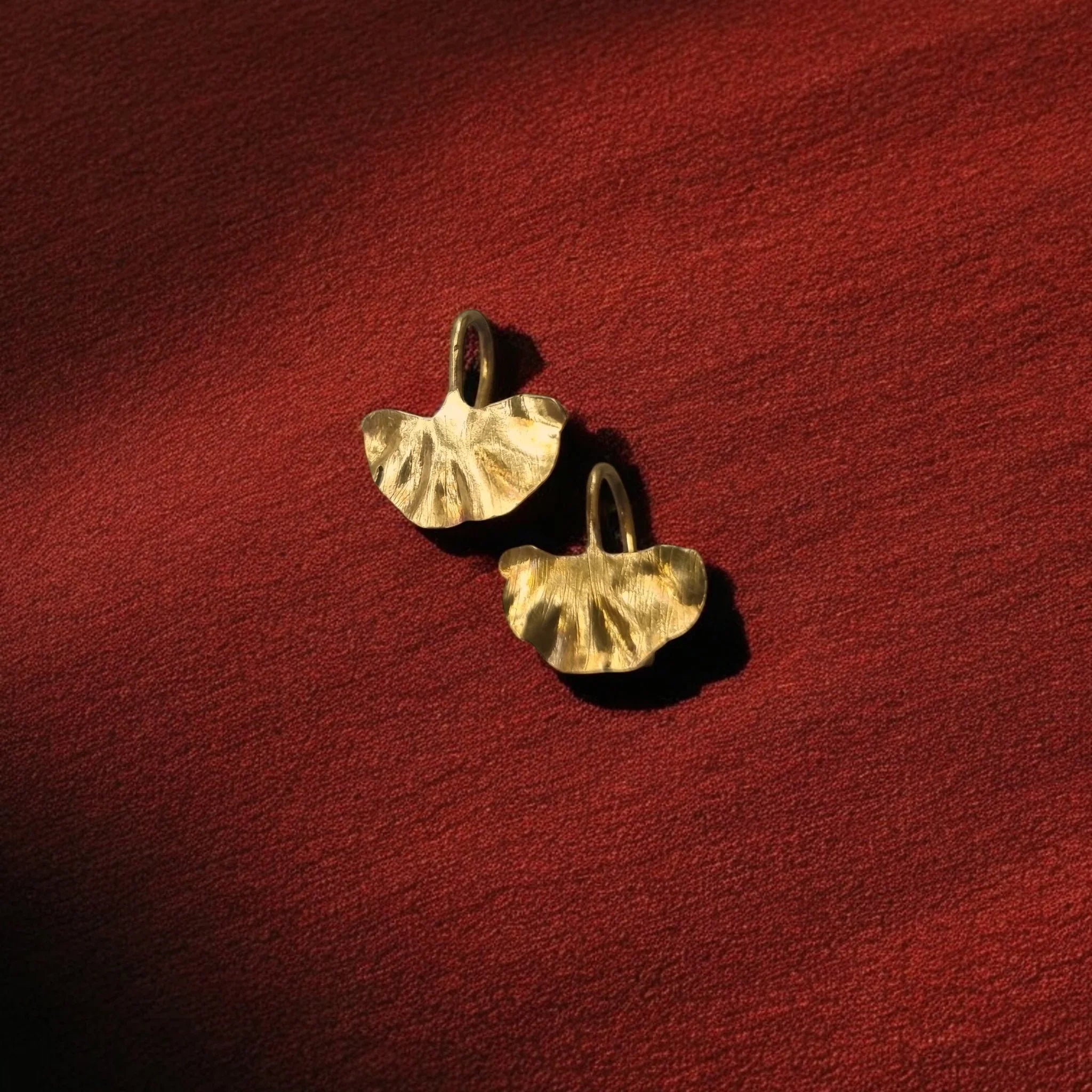 Pair of gold earrings on a red textured surface