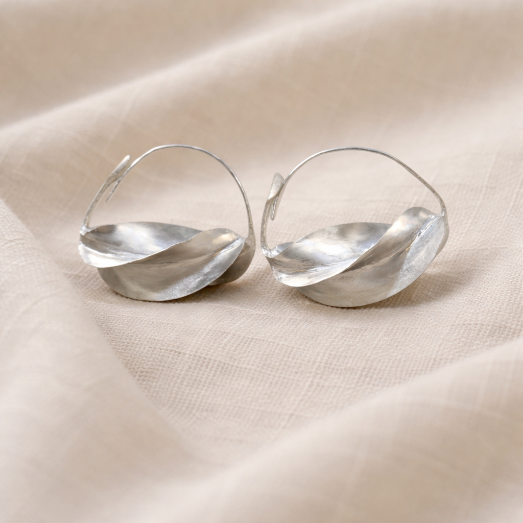 Pair of silver hoop earrings on a beige fabric background