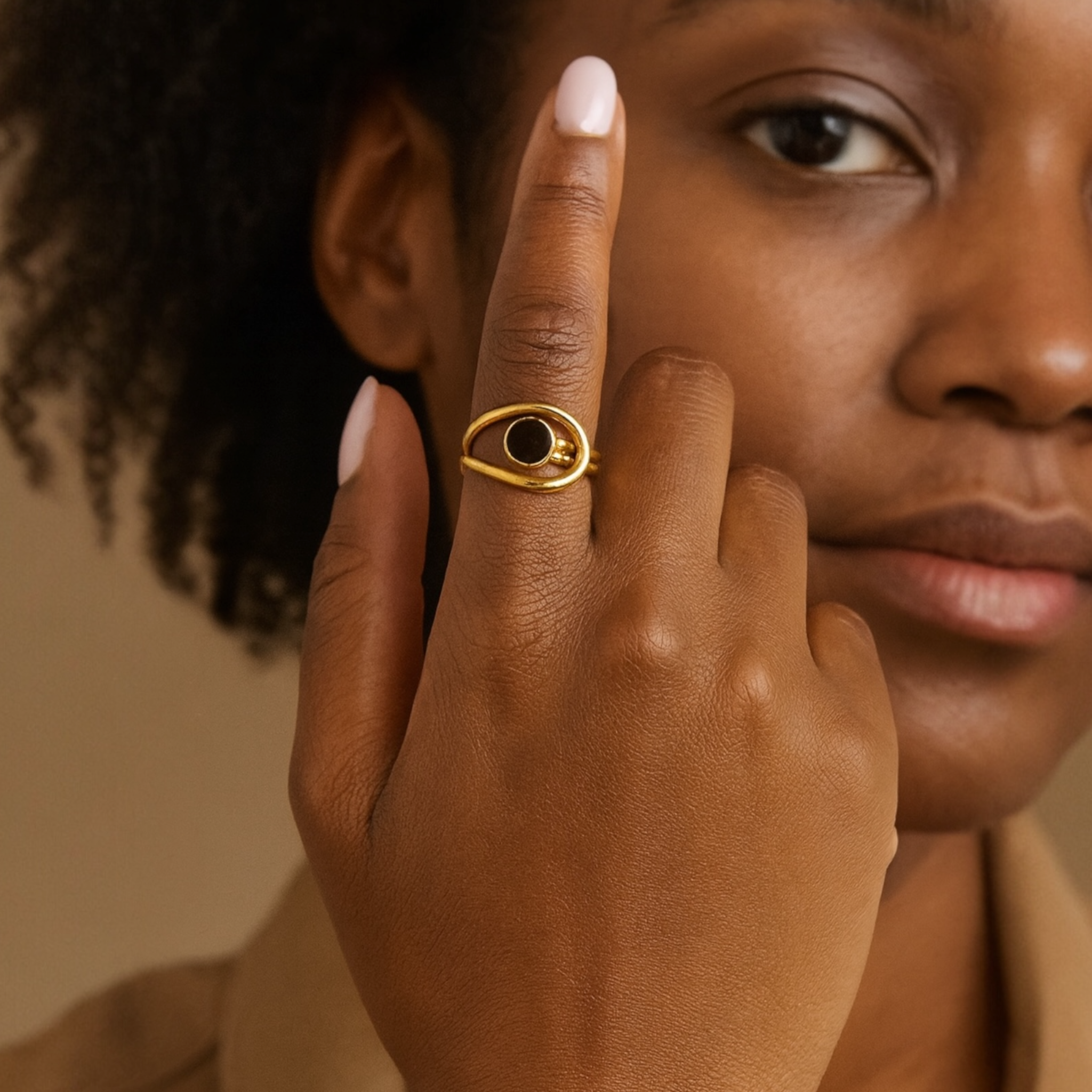 Close-up of a hand wearing a gold ring with a black stone, against a neutral background.