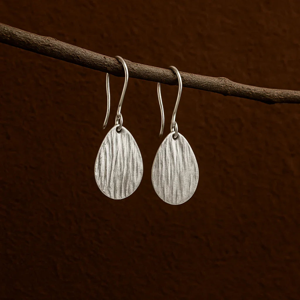 Silver teardrop earrings hanging on a branch against a brown background