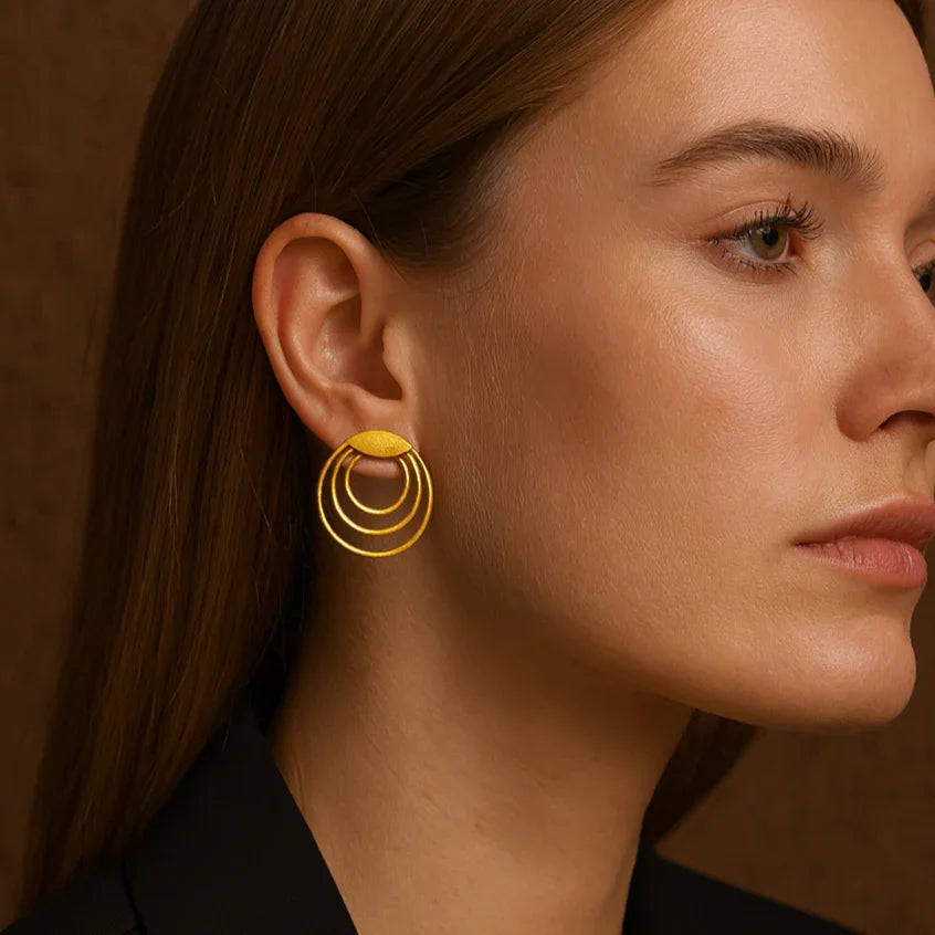 Woman wearing gold hoop earrings against a brown background