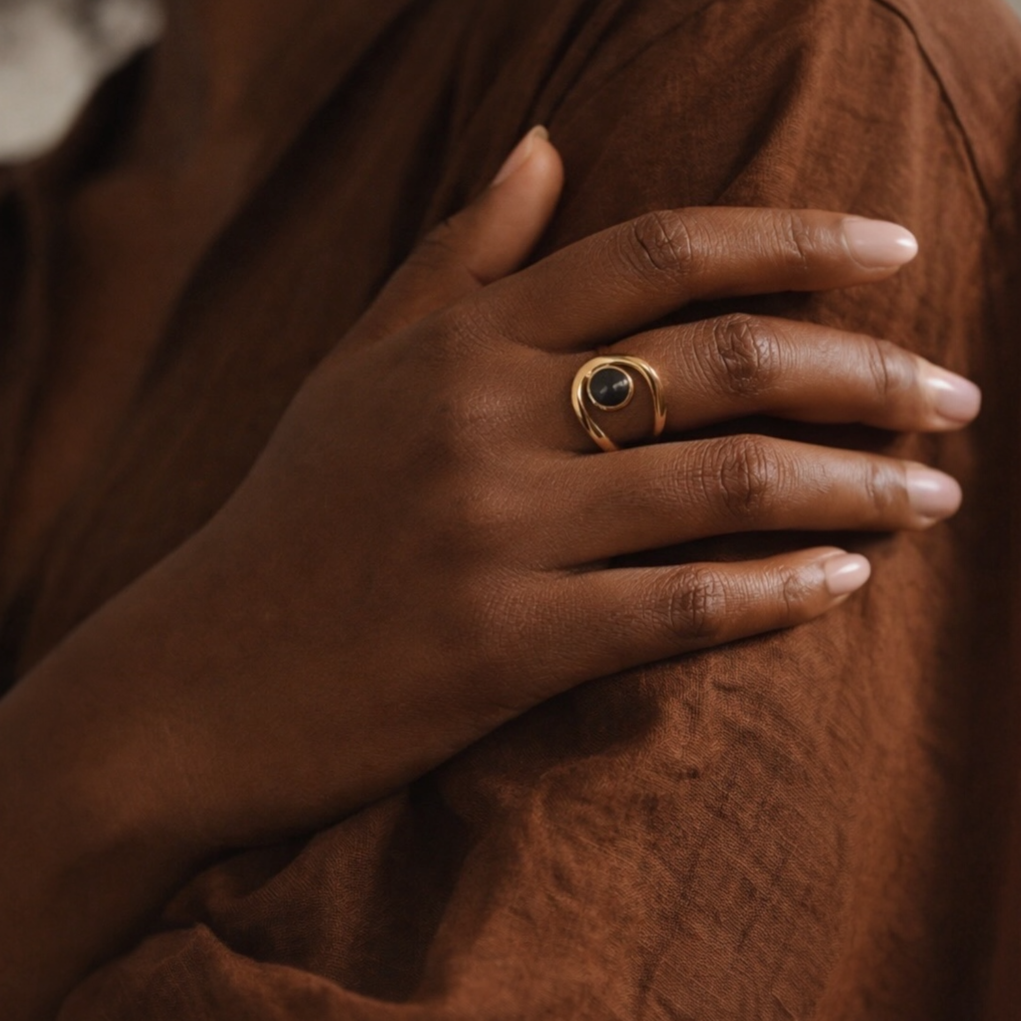 Hand wearing a gold ring with a dark gemstone on a brown textured background