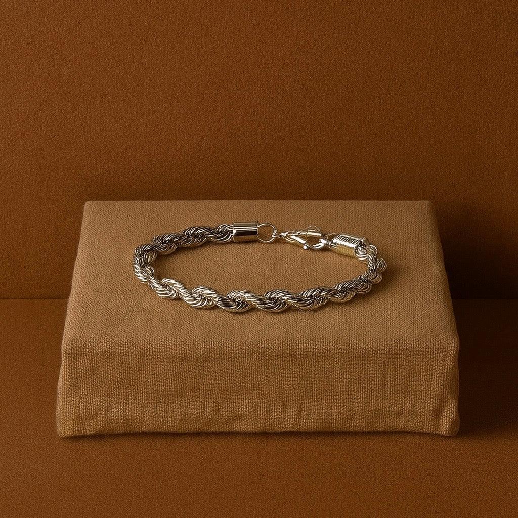 Silver braided bracelet on a brown fabric surface with a brown background