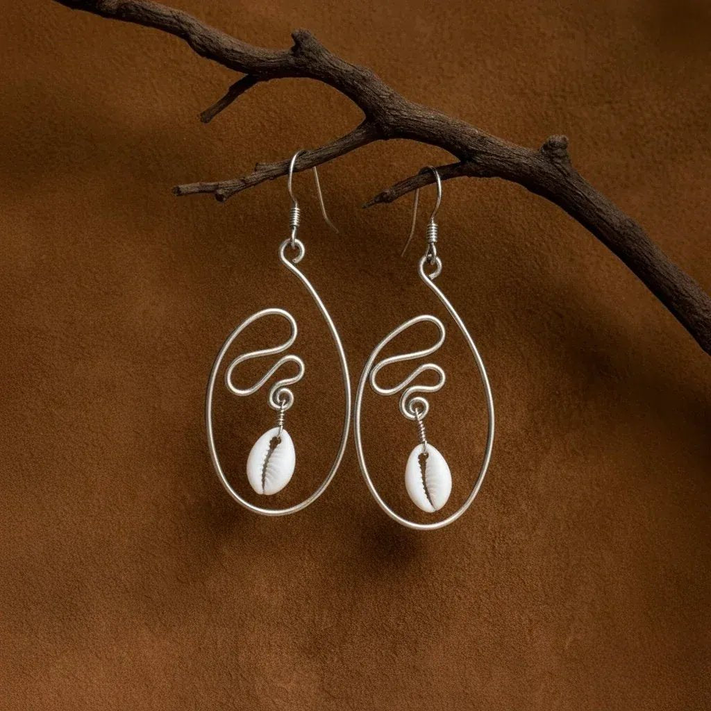 Pair of silver earrings with cowrie shells hanging on a branch against a brown background