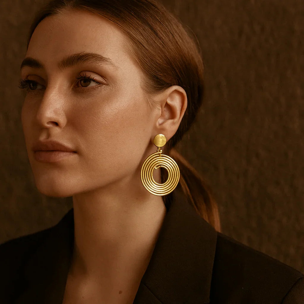 Woman wearing gold earrings against a brown background