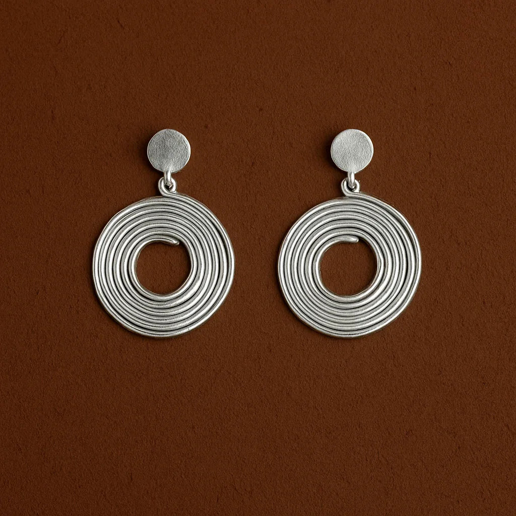 Pair of silver circular earrings on a brown background
