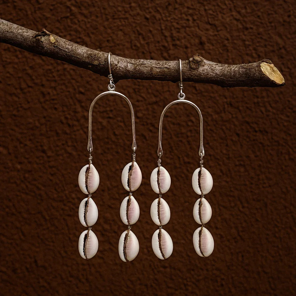 Pair of earrings with shell beads hanging from a branch against a brown background