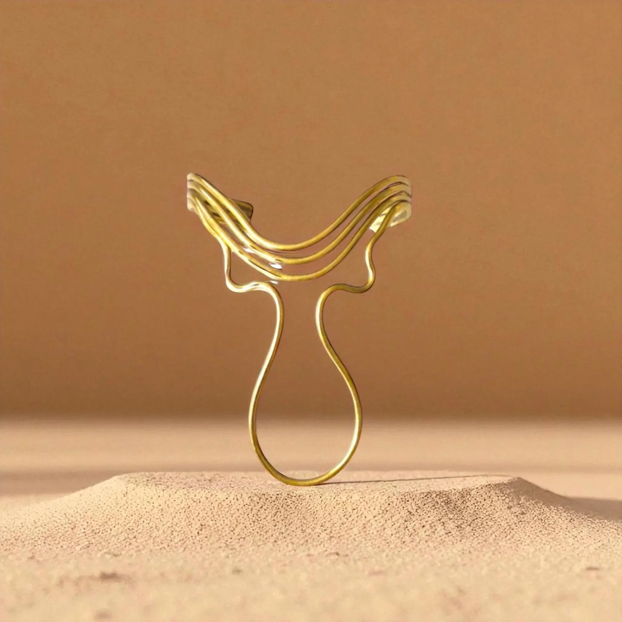 Gold decorative item resembling a horse head on a sand-like surface with a brown background