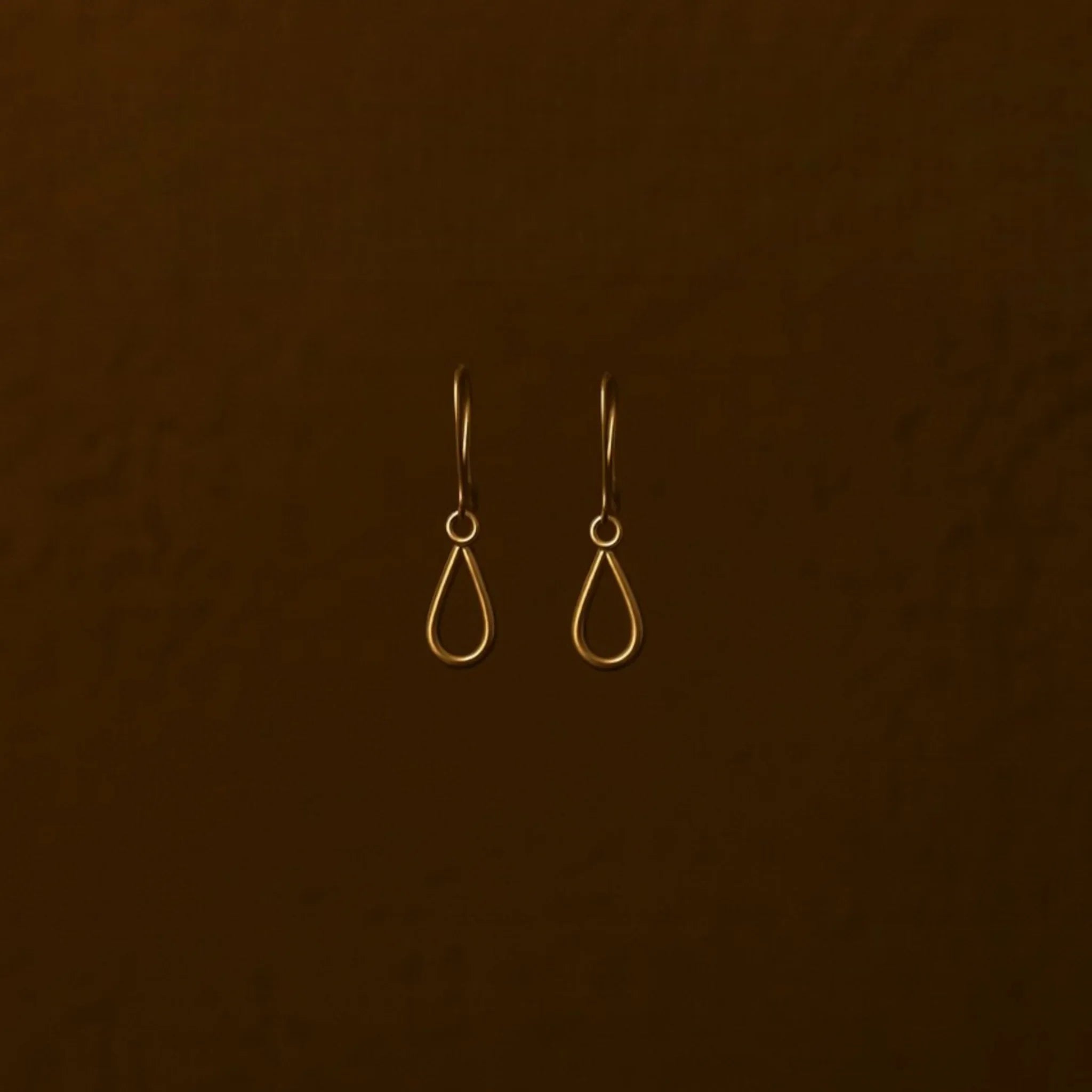 Pair of gold teardrop earrings on a brown background