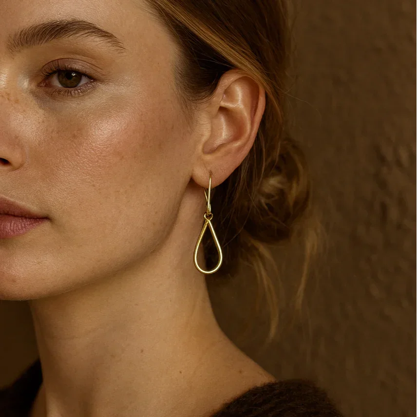Close-up of a woman wearing a gold earring against a brown background