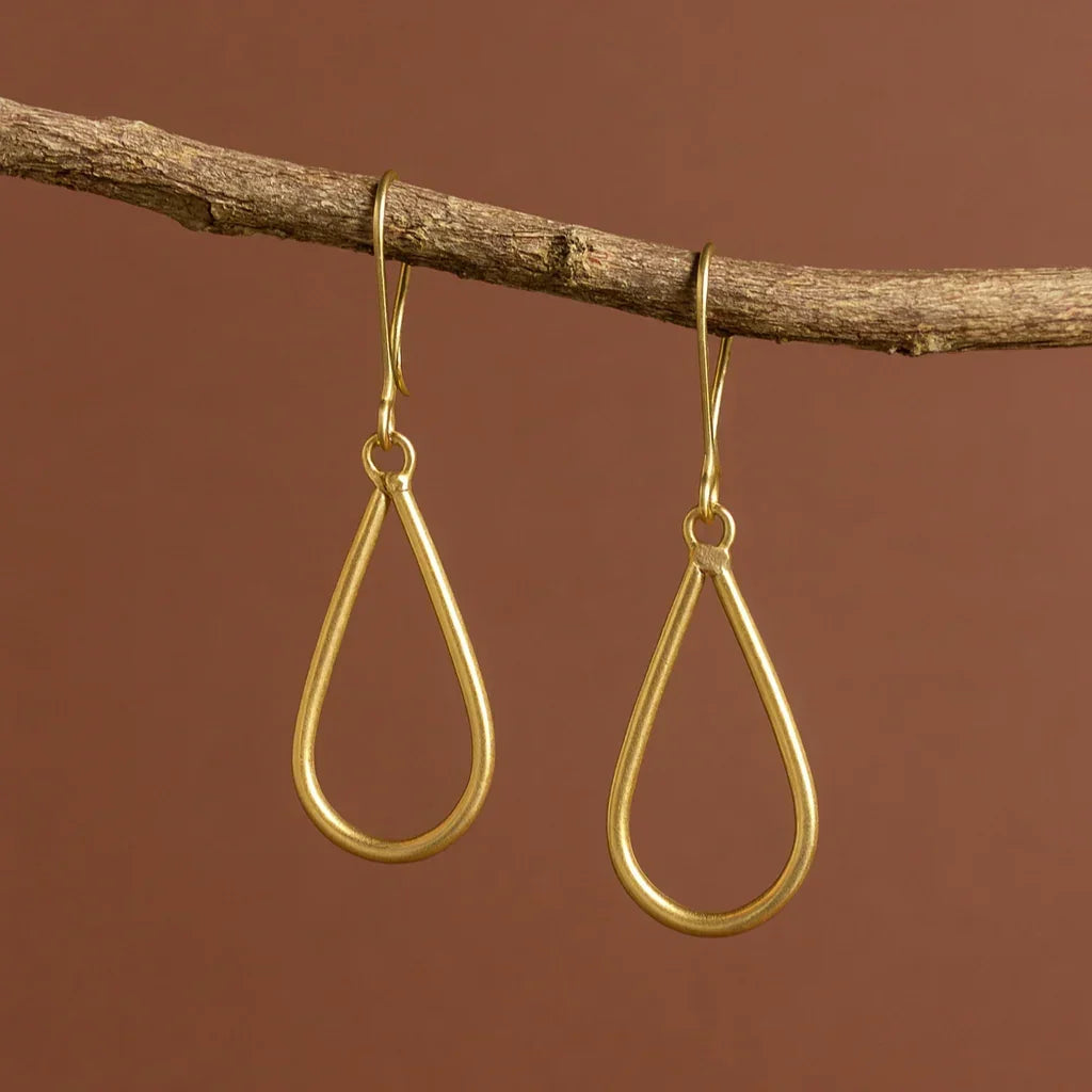 Gold teardrop earrings hanging from a branch against a brown background