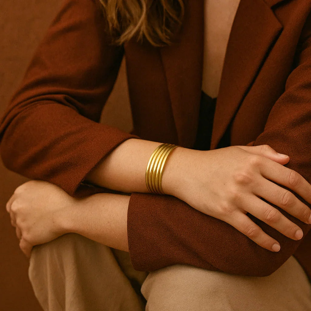 Woman wearing a brown blazer and gold bracelets against a warm-toned background
