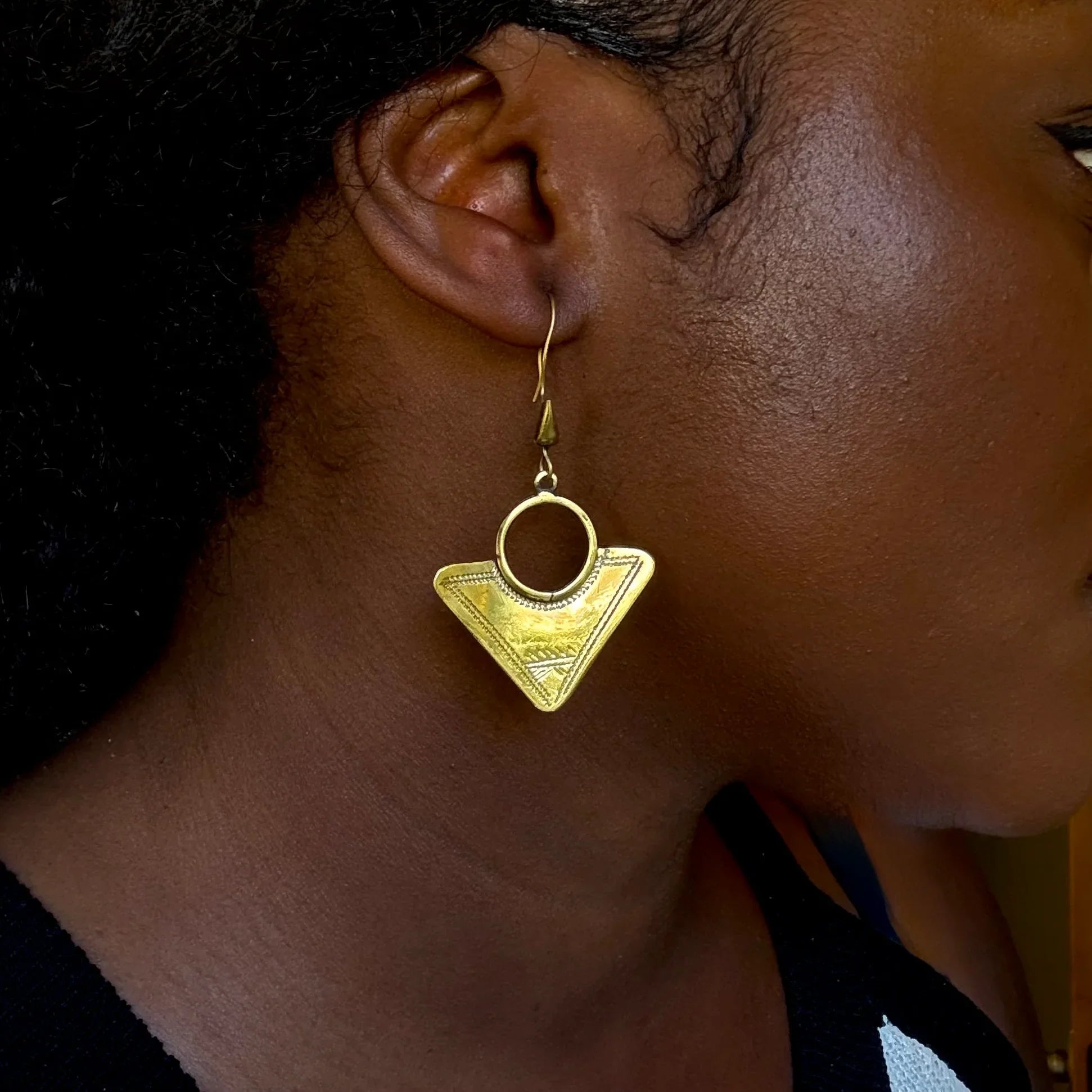 Gold triangle-shaped earring worn by a person