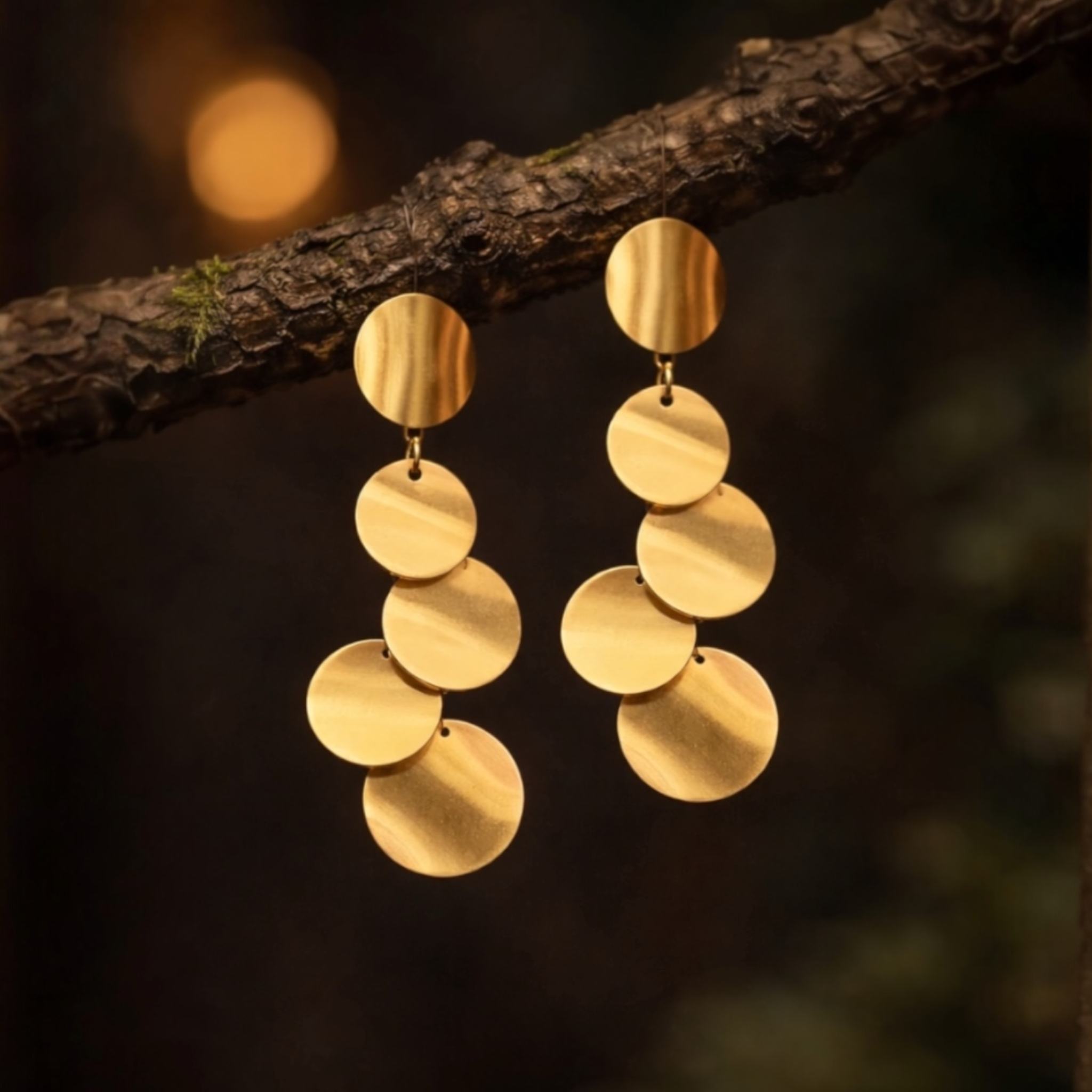 Gold disc earrings hanging on a branch with a blurred natural background