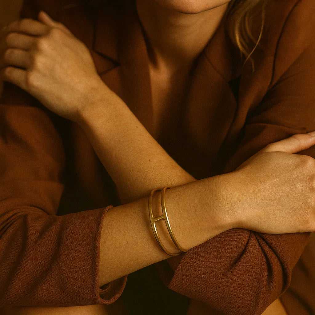 Woman wearing a brown outfit with gold bracelets against a warm-toned background