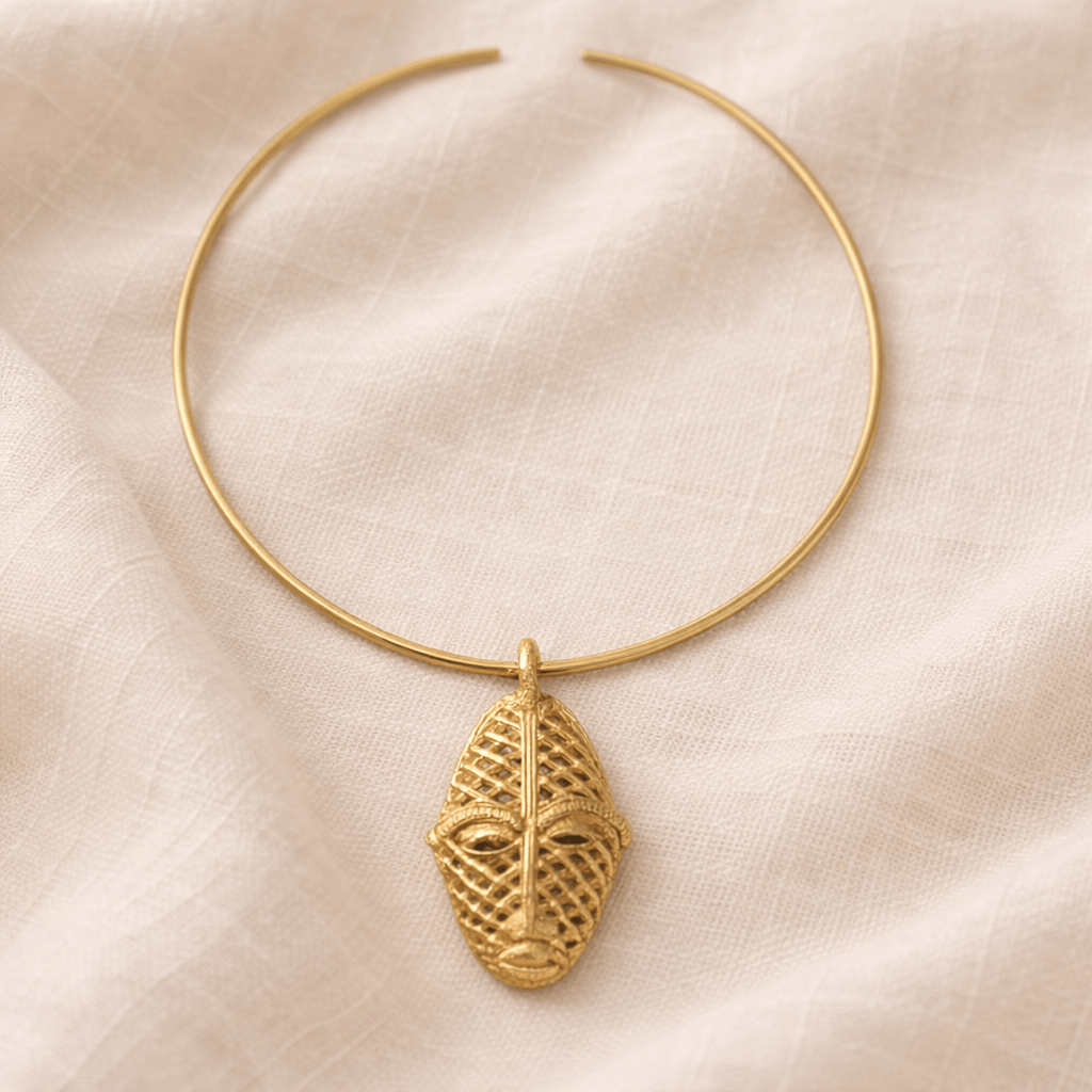Gold necklace with a face-shaped pendant on a beige fabric background