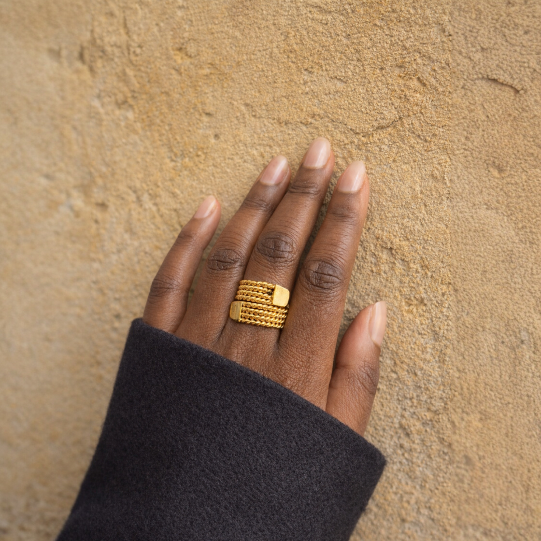Hand wearing a gold ring on a textured beige background