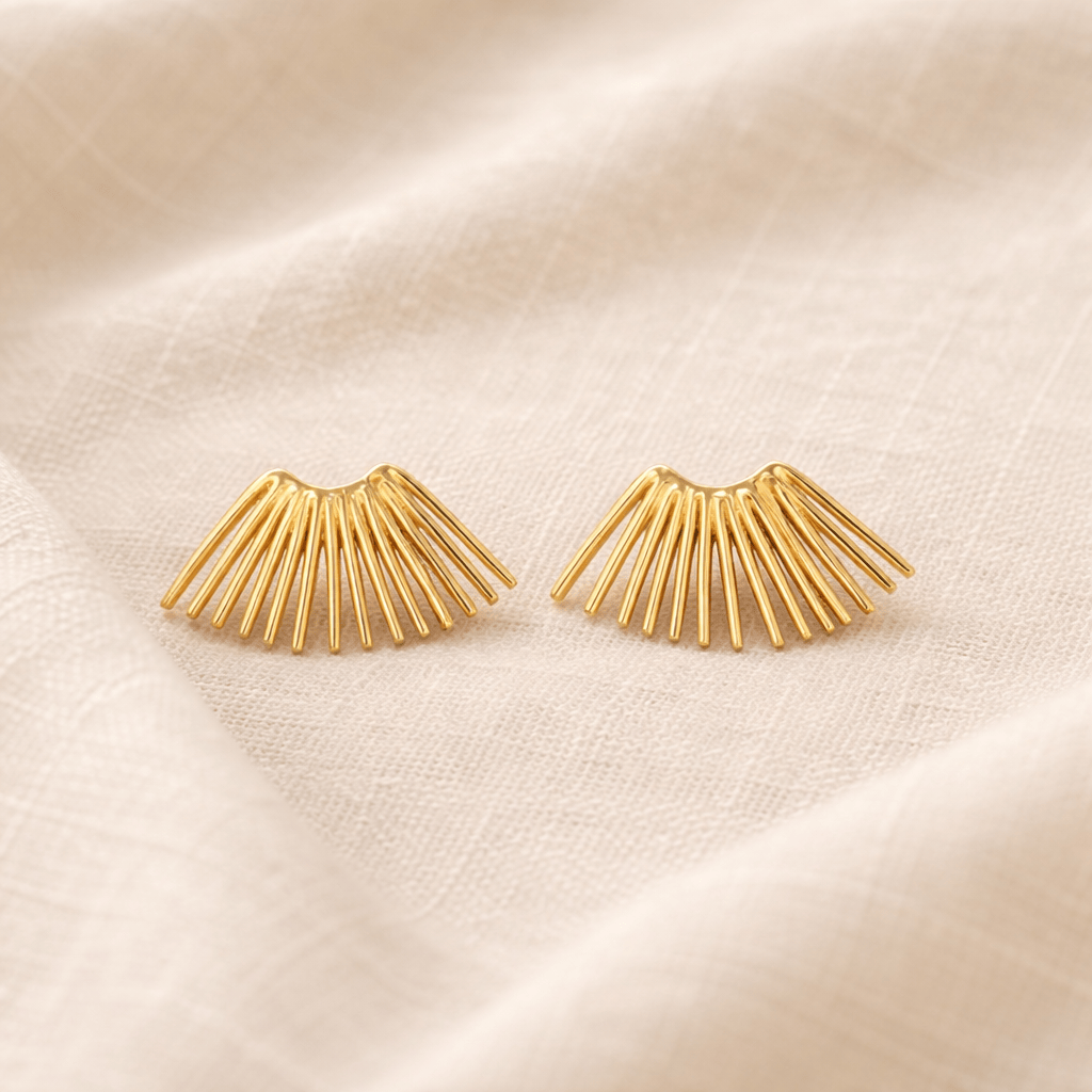 Gold fan-shaped earrings on a beige fabric background