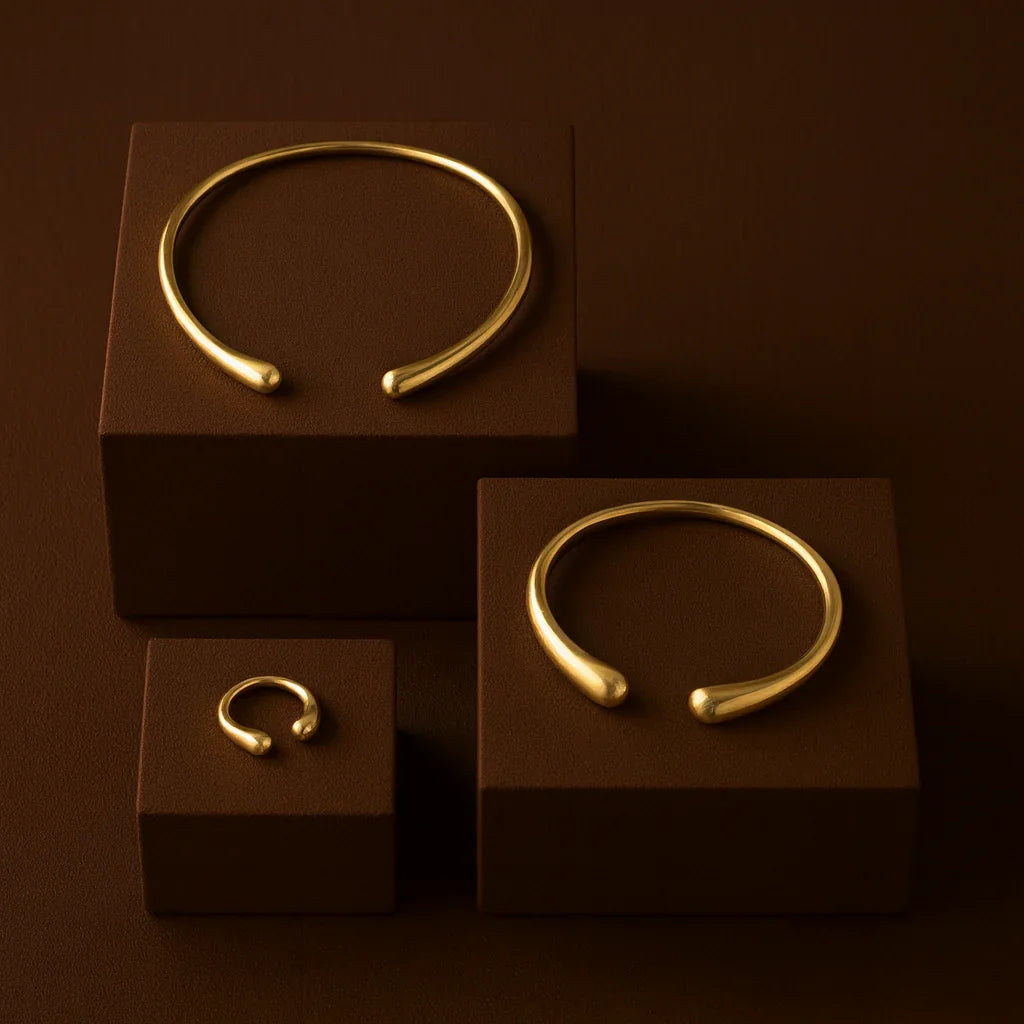 Three gold bracelets on brown stands against a dark brown background