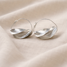 Pair of silver hoop earrings on a beige fabric background