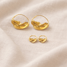 Pair of gold hoop earrings on a beige fabric background
