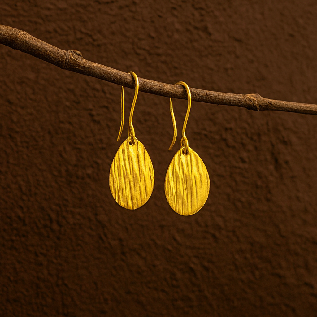 Gold earrings hanging on a branch against a brown background