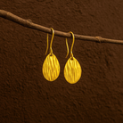 Gold earrings hanging on a branch against a brown background