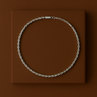 Silver chain necklace on a brown square platform with a brown background