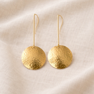 Pair of gold earrings on a beige fabric background