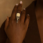 Hand wearing a ring with a face design on a brown background