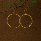 Gold hoop earrings with snake heads on a brown textured background