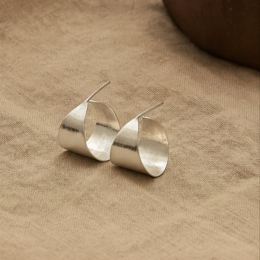 Pair of silver earrings on a beige fabric background