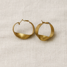 Pair of gold hoop earrings on a textured beige surface