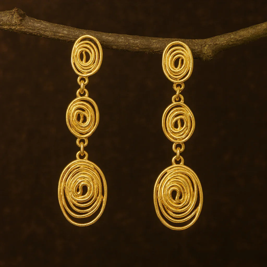 Pair of gold spiral earrings hanging from a branch on a dark brown background