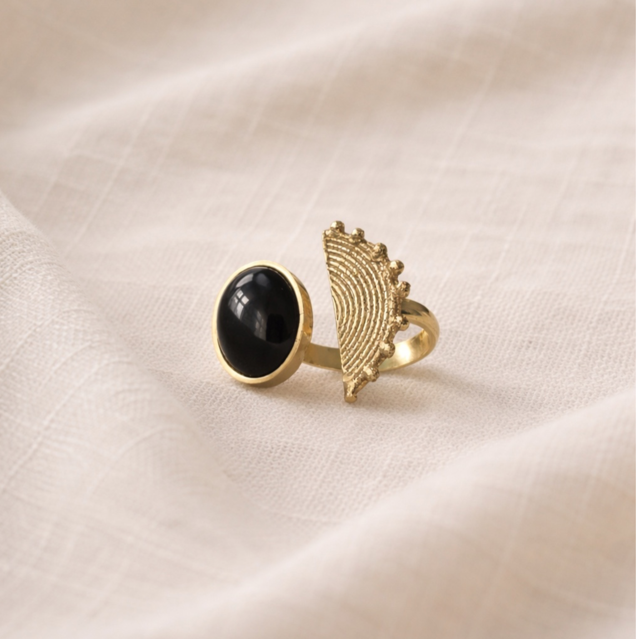 Gold ring with black gemstone on a beige fabric background