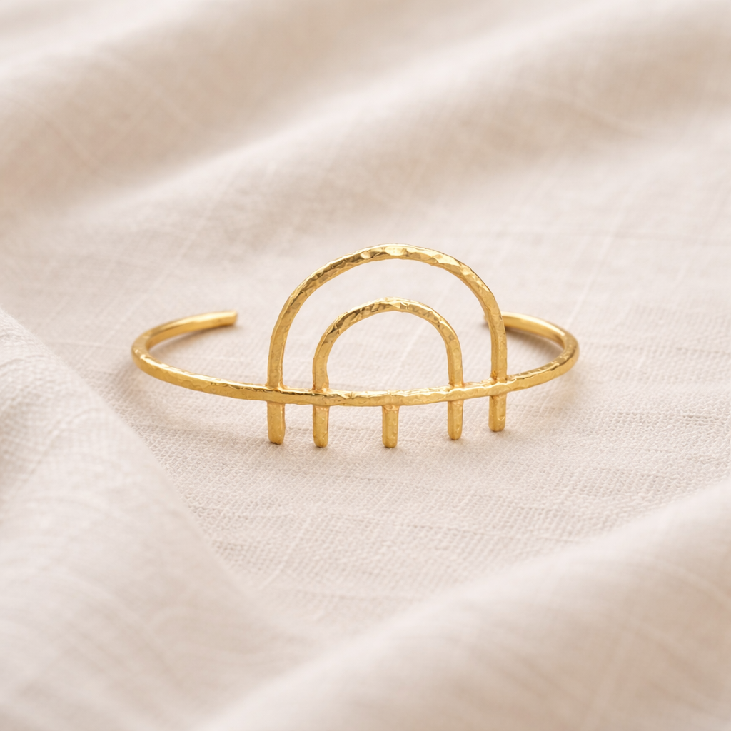 Gold bracelet with arch design on a beige fabric background