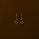 Pair of gold teardrop earrings on a brown background