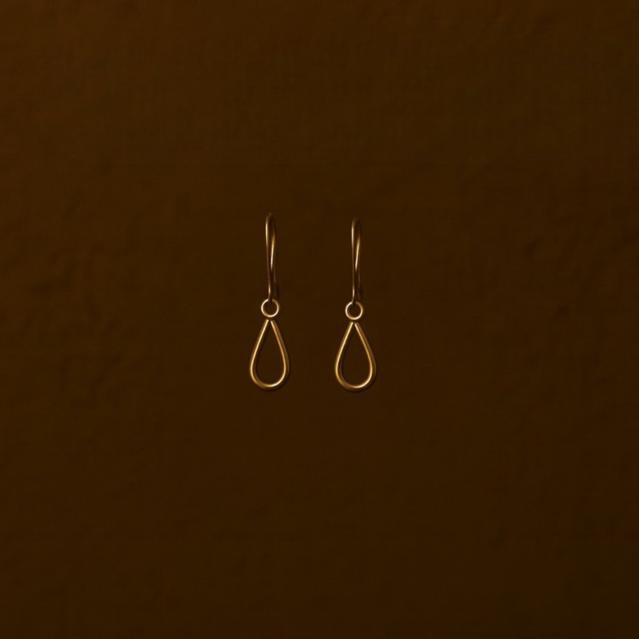 Pair of gold teardrop earrings on a brown background