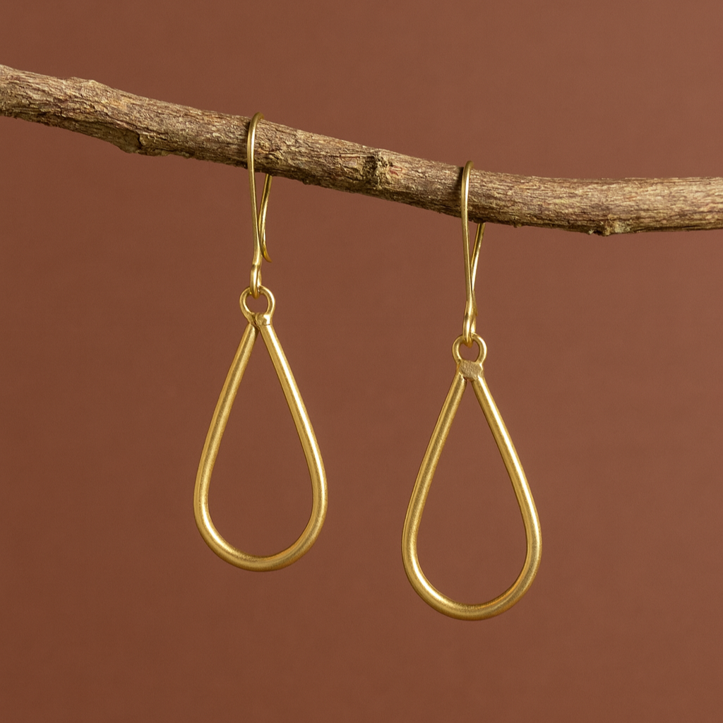 Gold teardrop earrings hanging from a branch against a brown background