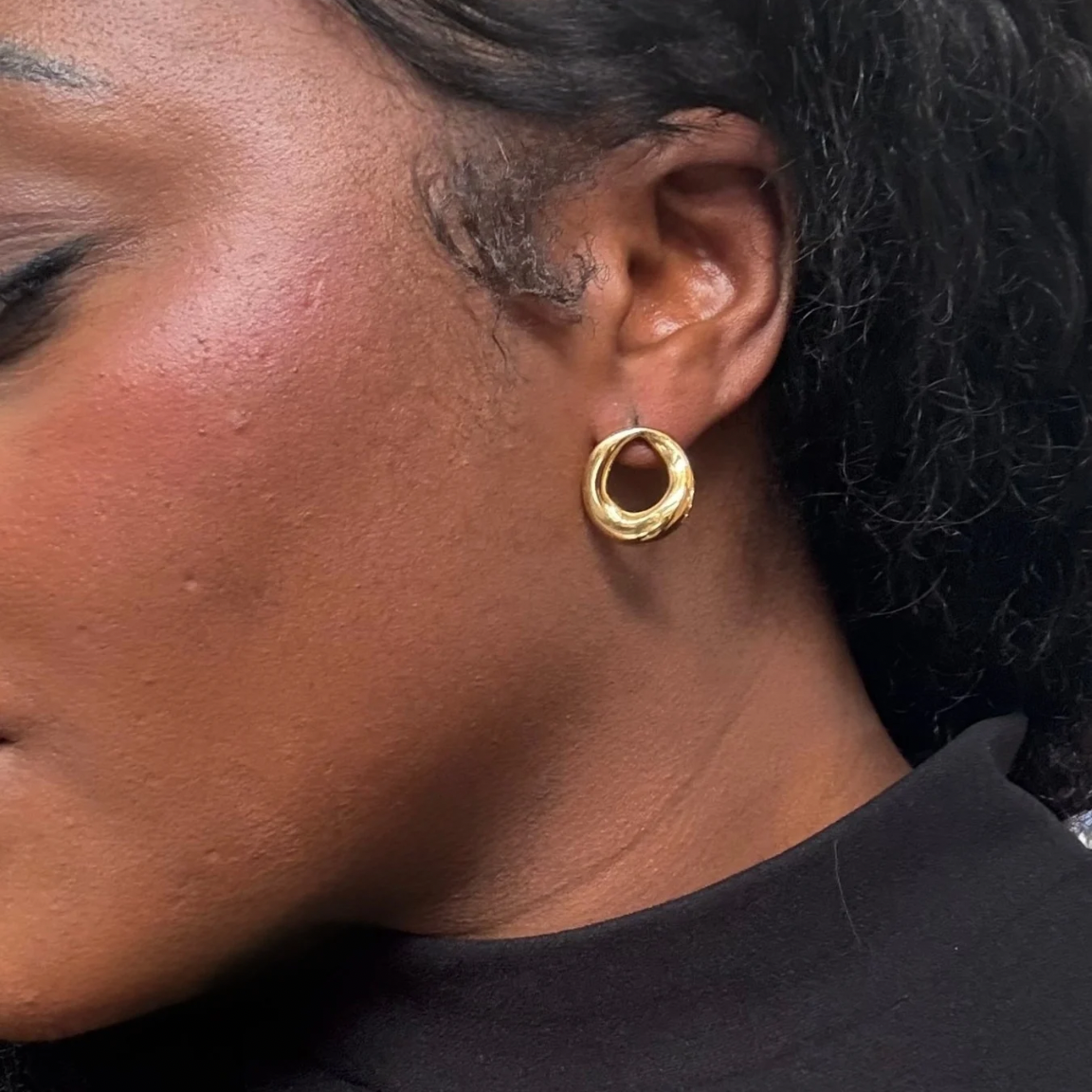 Close-up of a person wearing a gold hoop earring.