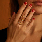 Close-up of a hand wearing a gold ring with a unique design, against a warm-toned background.