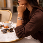 Woman sitting at a cafe table with a cup of coffee, croissant, and sunglasses.
