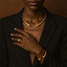Person wearing a black blazer with gold jewelry on a brown background