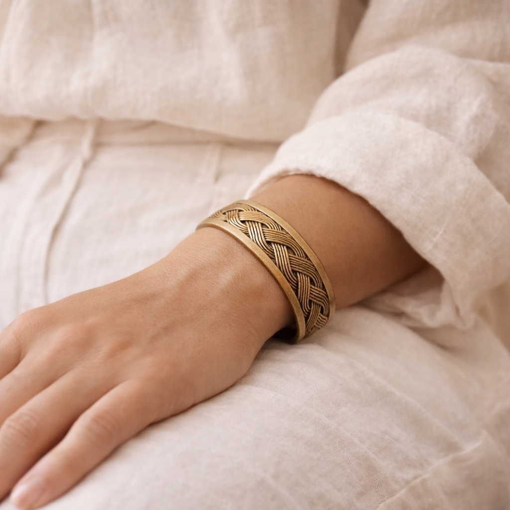 Gold braided bracelet on a wrist with a soft beige background
