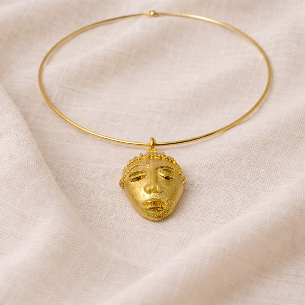 Gold necklace with a face-shaped pendant on a beige fabric background