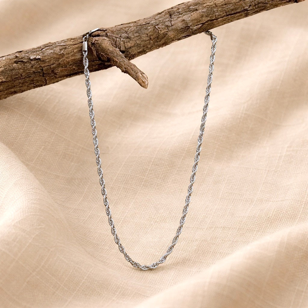 Silver chain necklace on a wooden branch with a beige fabric background