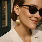 Woman wearing sunglasses and gold earrings with a blurred background